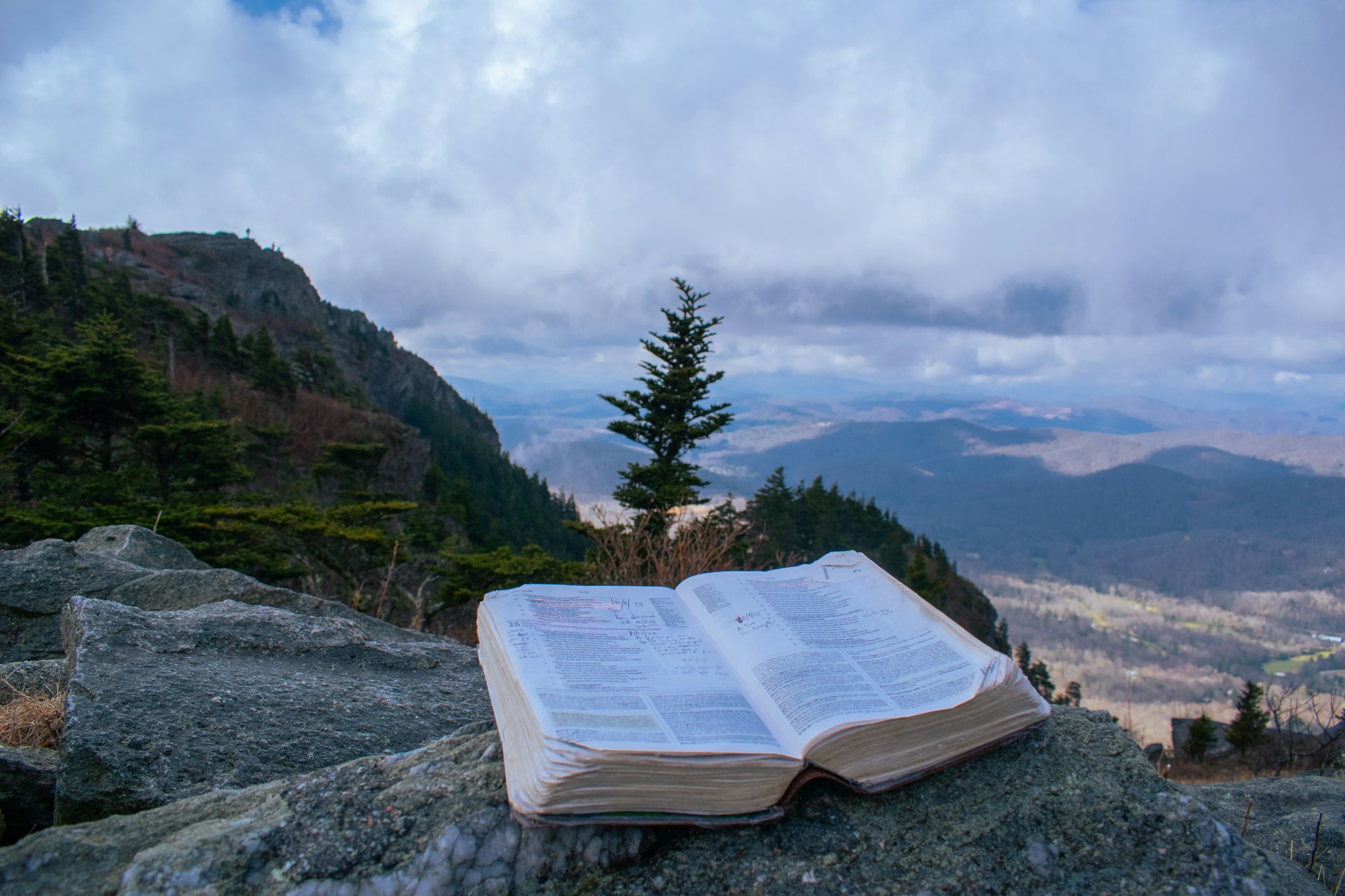 Open bible rests on rocks with mountain vista background